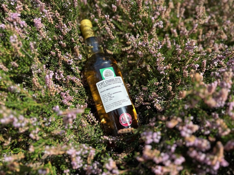 Bottle of Oakwood Whisky's Port Charlotte, resting on a bed of heather.